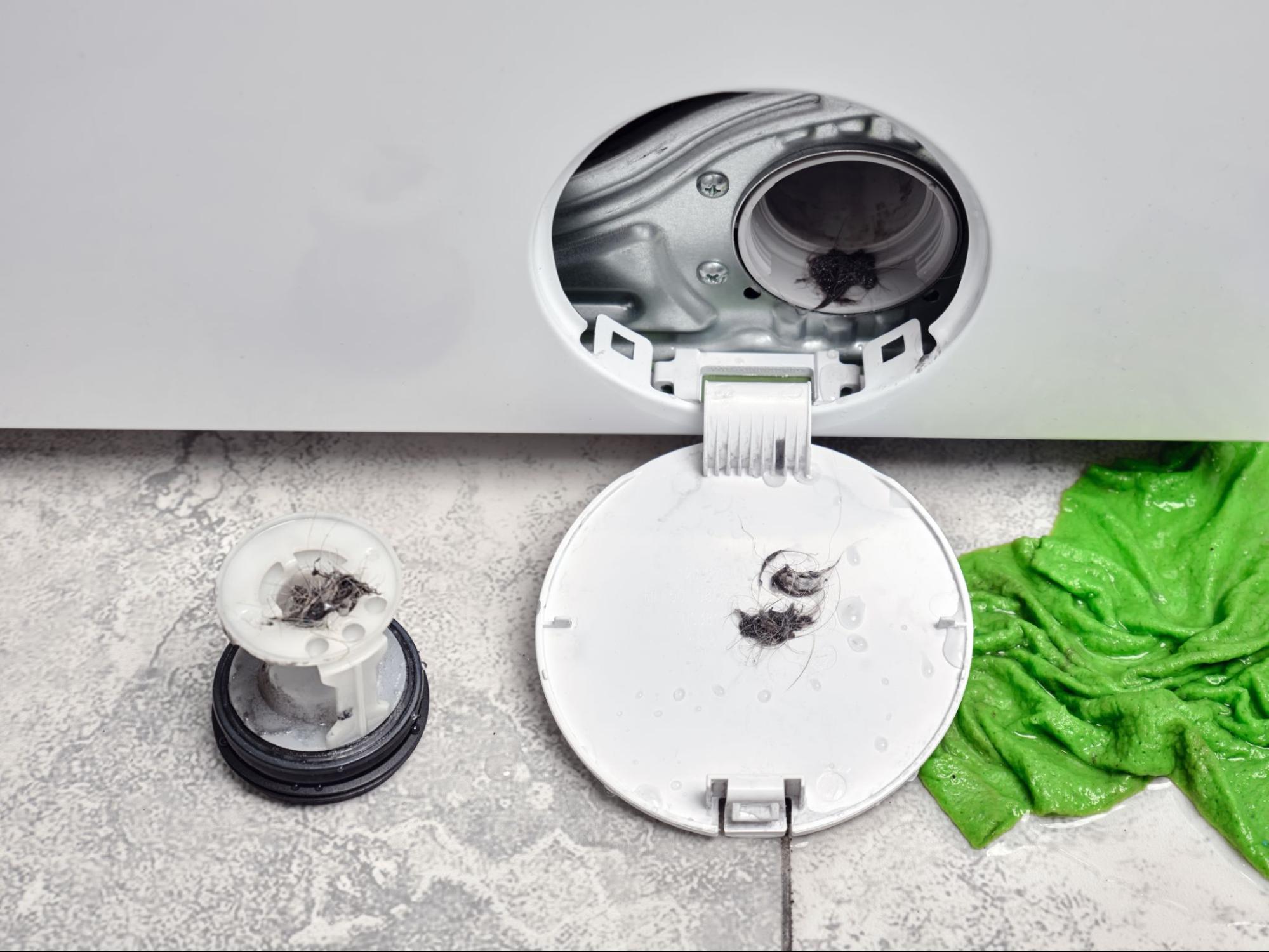 Verstopte wasmachinefilter met opgehoopt vuil na het openen van het serviceluik