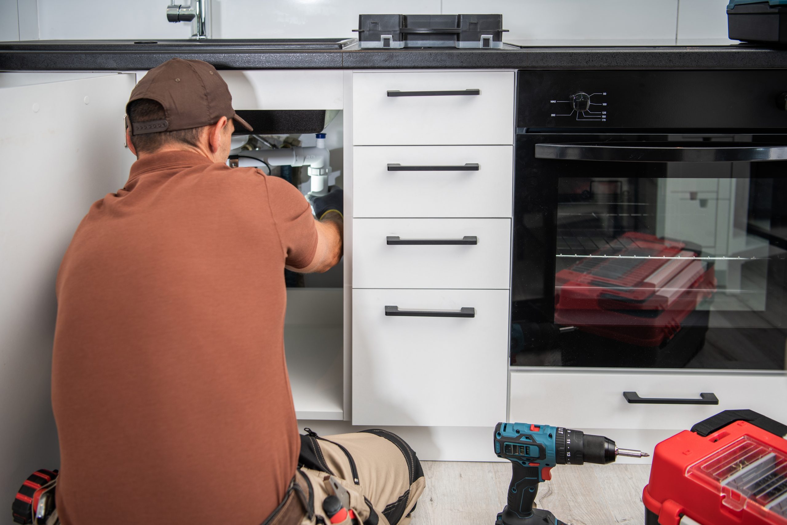 Professionele loodgieter die een afvoer ontstoppt in de keuken, waarbij de prijs afhangt van techniek en ernst van de verstopping