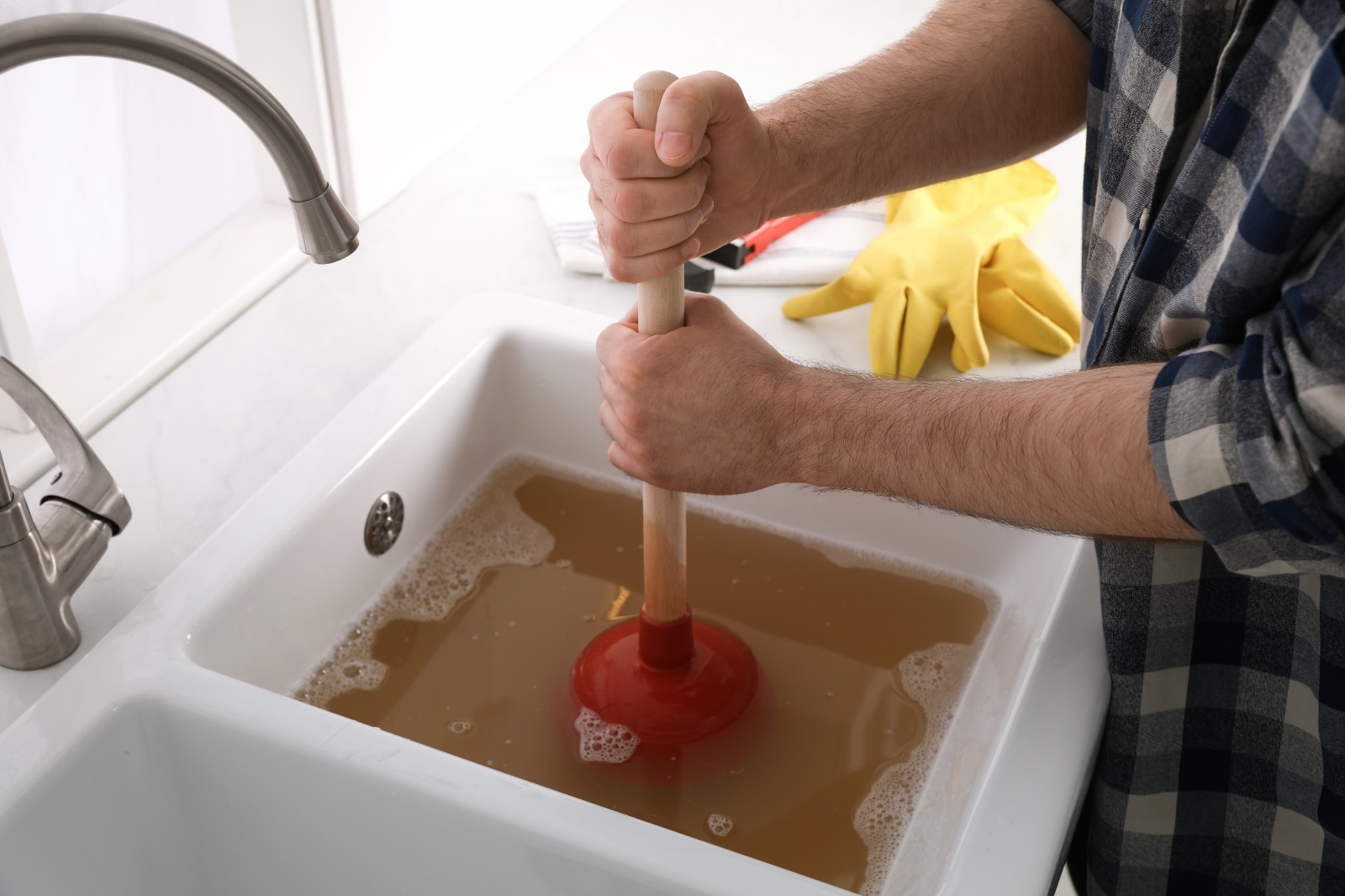 Gootsteen ontstoppen met een rode plopper in een spoelbak vol vuil water.