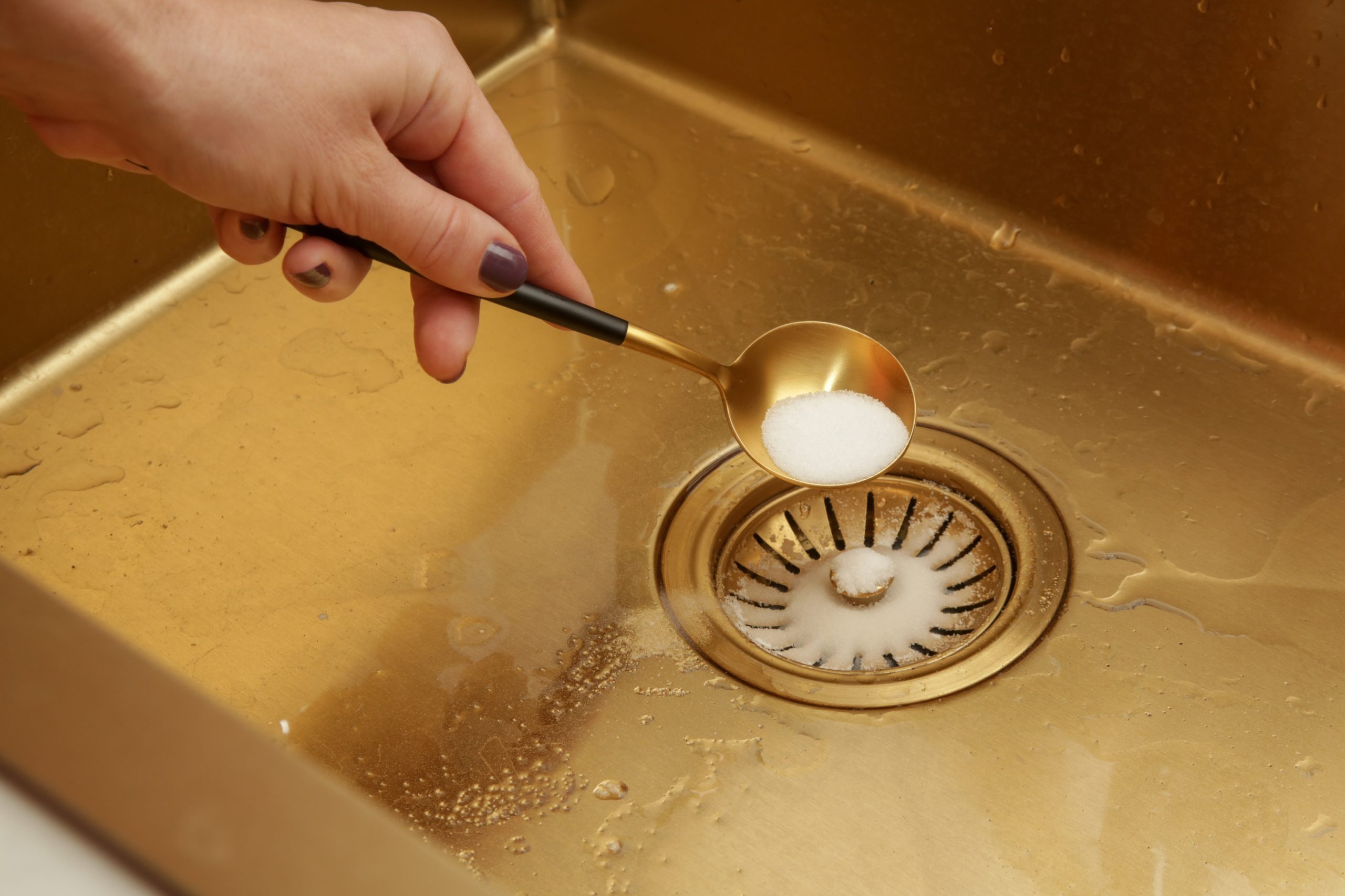 Persoon strooit baking soda in de keukenafvoer als preventieve tip om verstoppingen in de keuken te voorkomen