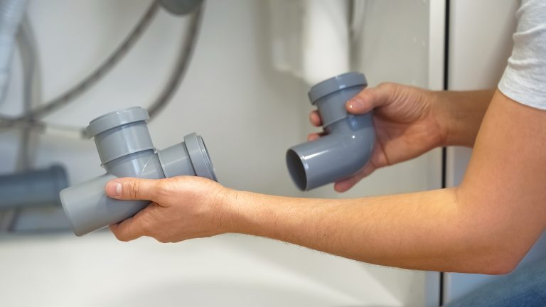 Professionele loodgieter controleert de afvoerleidingen onder de gootsteen om een hardnekkige keukenverstopping te verhelpen