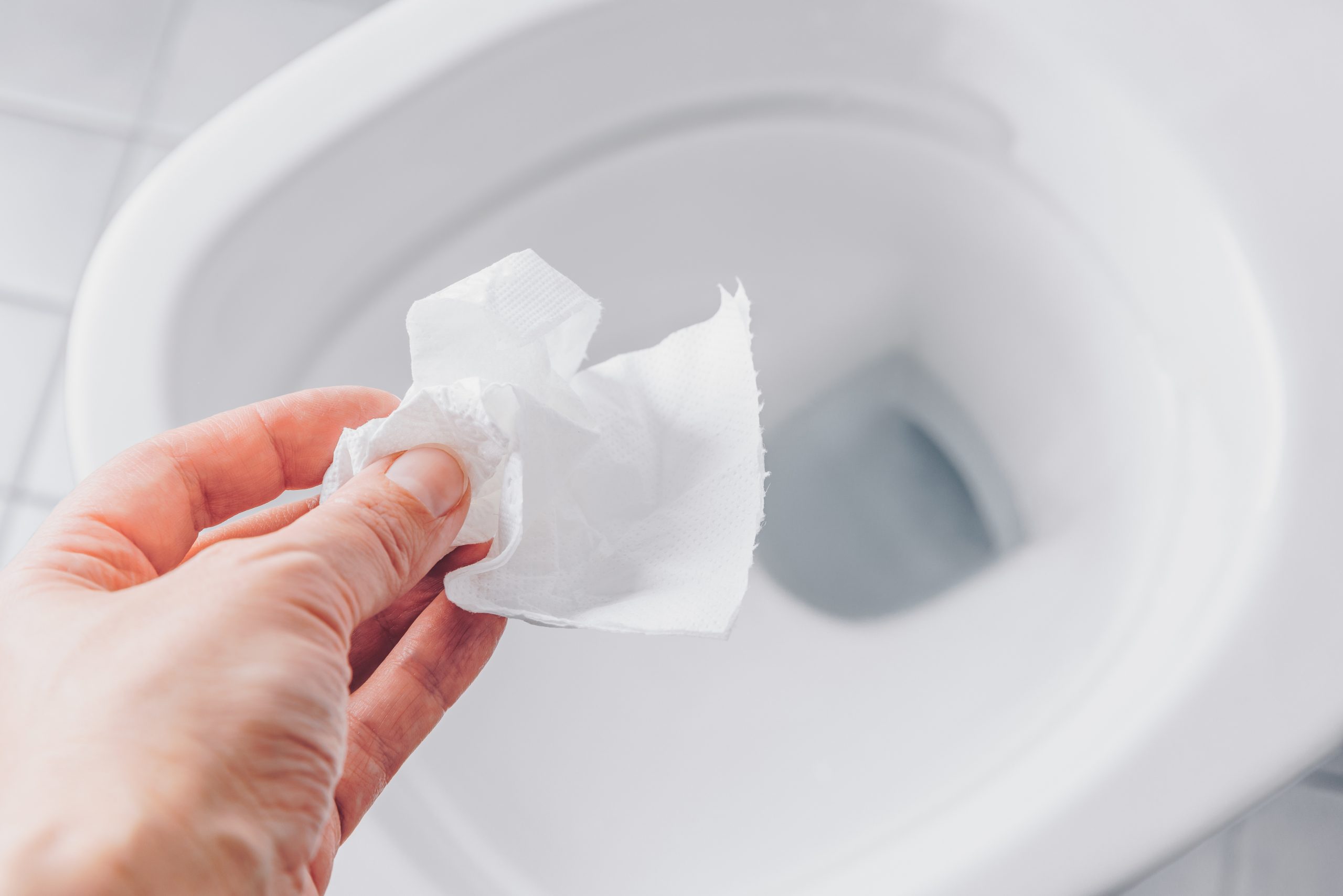 Hand die een vochtig doekje boven een toilet houdt — een veelvoorkomende oorzaak van een verstopt toilet.